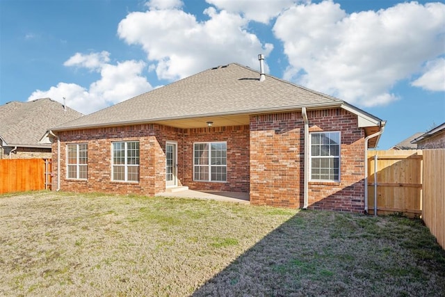 rear view of house with a yard, brick siding, a fenced backyard, and a shingled roof