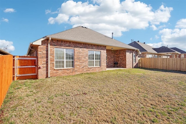 rear view of house featuring brick siding, a lawn, a shingled roof, and a fenced backyard