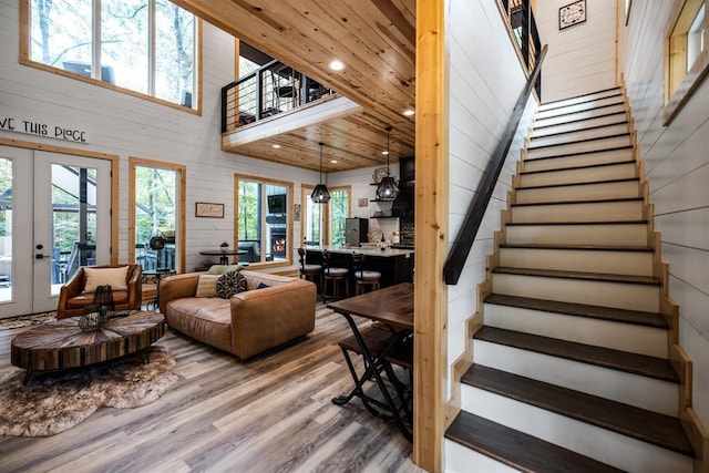 living area featuring wooden walls, a towering ceiling, stairs, french doors, and light wood finished floors