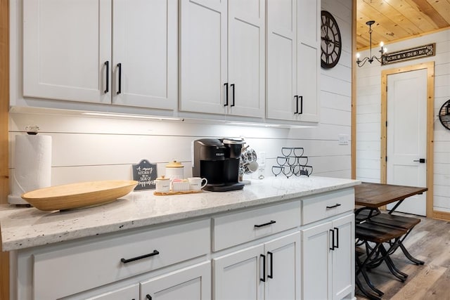 kitchen featuring wooden walls, white cabinets, wood ceiling, light stone countertops, and light wood-style floors