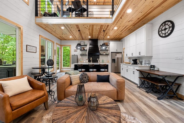 living room with wooden ceiling, wooden walls, recessed lighting, a towering ceiling, and light wood-style floors