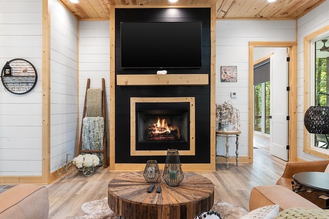 living room featuring wooden ceiling, a warm lit fireplace, and wood finished floors