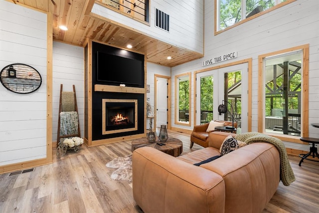 living room featuring wooden ceiling, wood walls, a fireplace, wood finished floors, and visible vents