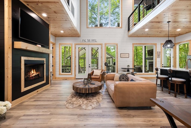 living area with light wood-type flooring, a warm lit fireplace, wooden ceiling, and french doors