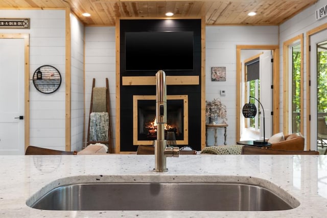 interior space featuring a warm lit fireplace, wood ceiling, light stone counters, and wood walls