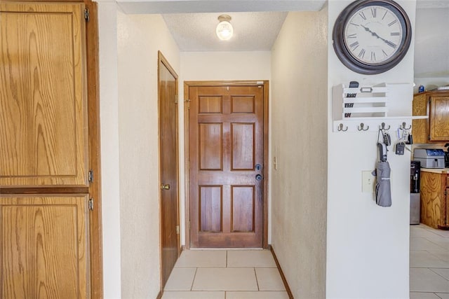 doorway with light tile patterned floors, a textured wall, and a textured ceiling