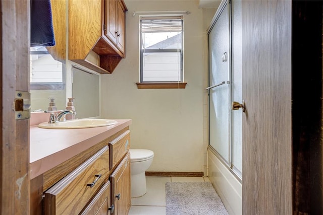 bathroom featuring toilet, shower / bath combination with glass door, tile patterned flooring, baseboards, and vanity