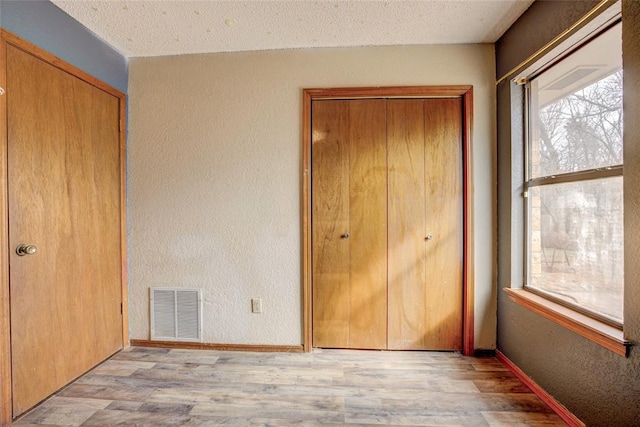 unfurnished bedroom with visible vents, multiple windows, a textured wall, and wood finished floors