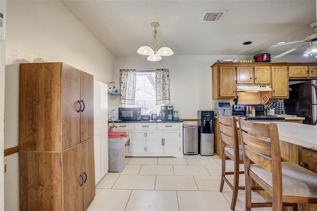 kitchen with visible vents, pendant lighting, under cabinet range hood, black microwave, and ceiling fan with notable chandelier