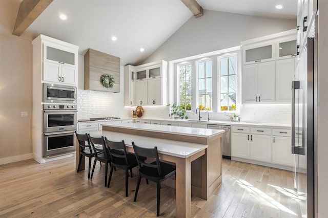 kitchen with lofted ceiling with beams, light countertops, appliances with stainless steel finishes, light wood-style floors, and white cabinetry