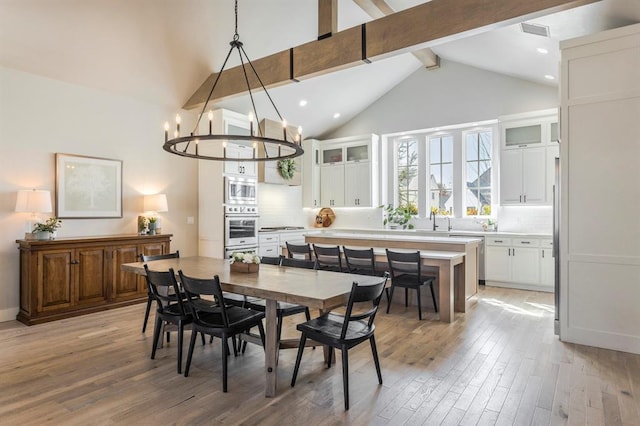 dining space with visible vents, light wood-type flooring, beam ceiling, a notable chandelier, and high vaulted ceiling