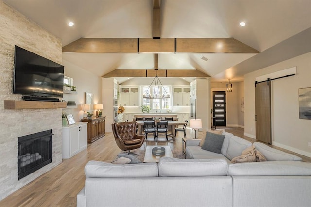 living area featuring a stone fireplace, a barn door, vaulted ceiling with beams, and light wood-type flooring