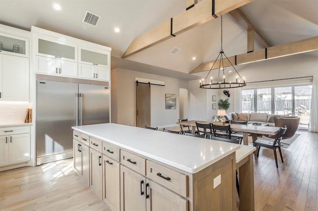 kitchen featuring visible vents, lofted ceiling with beams, a kitchen island, built in fridge, and a barn door