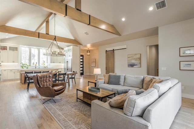 living area featuring visible vents, an inviting chandelier, a barn door, beamed ceiling, and light wood-type flooring