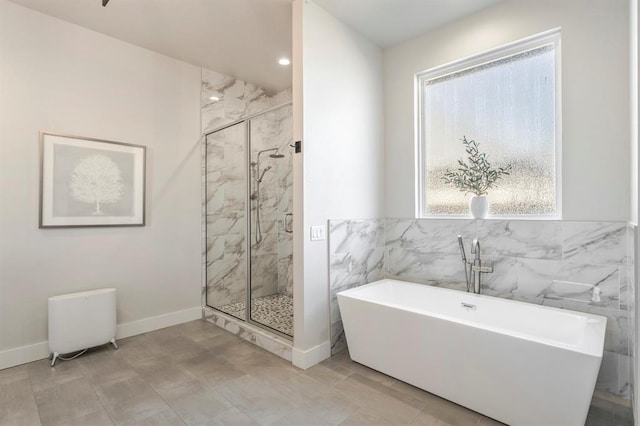 full bathroom with a freestanding tub, a marble finish shower, baseboards, and tile walls