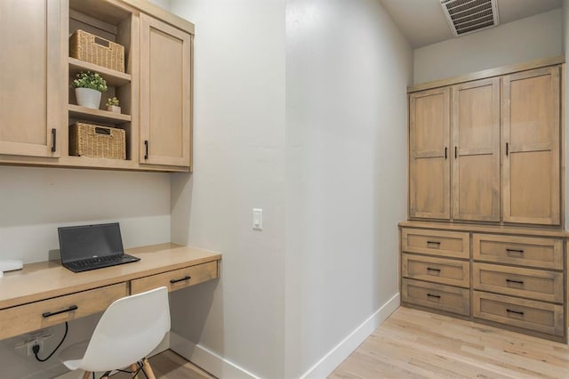 home office featuring light wood-type flooring, visible vents, built in desk, and baseboards