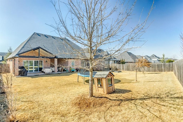 view of yard featuring a trampoline, a fenced backyard, and a patio area