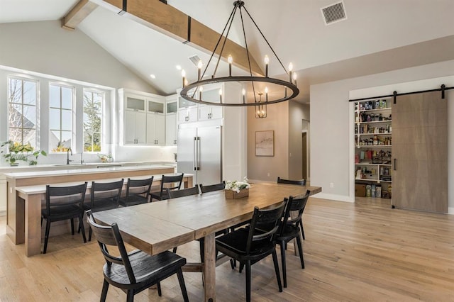 dining area with light wood-style flooring, beam ceiling, high vaulted ceiling, a chandelier, and a barn door
