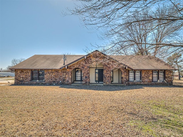 ranch-style home featuring stone siding and a front lawn