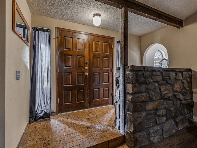 entryway featuring brick floor, beamed ceiling, and a textured ceiling