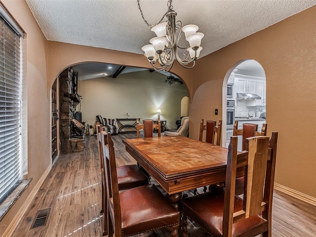 dining space with visible vents, arched walkways, wood finished floors, and a chandelier