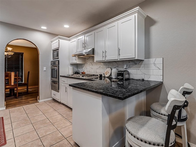 kitchen with tasteful backsplash, under cabinet range hood, appliances with stainless steel finishes, a peninsula, and arched walkways