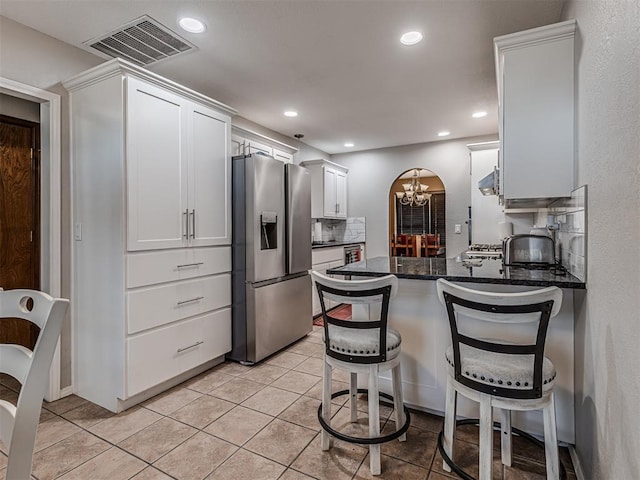 kitchen with visible vents, stainless steel fridge, arched walkways, a peninsula, and white cabinets