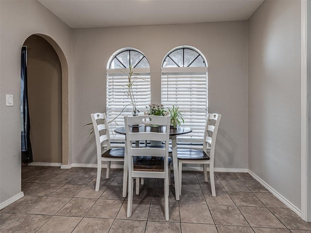 tiled dining space featuring baseboards and arched walkways