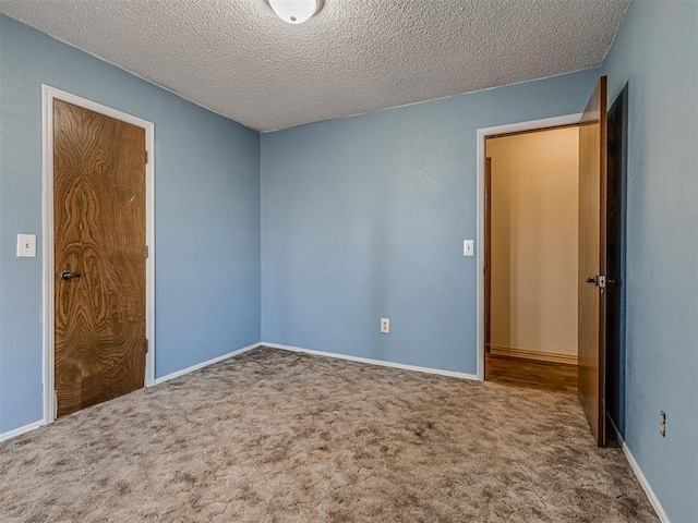 carpeted spare room featuring a textured ceiling and baseboards