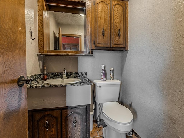 bathroom with vanity, toilet, and a textured wall