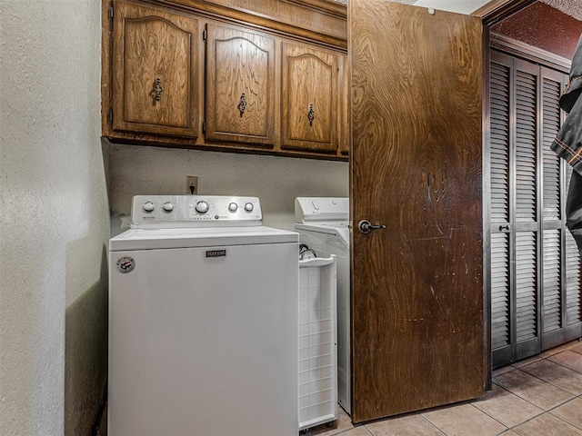 laundry room featuring light tile patterned floors, cabinet space, a textured wall, and washer and clothes dryer