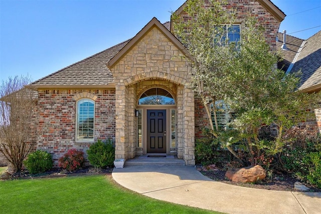 property entrance featuring brick siding, stone siding, a yard, and roof with shingles