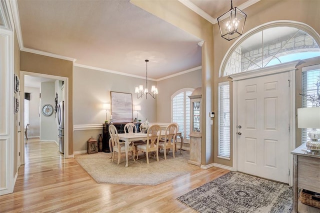 entryway with a notable chandelier, light wood-style flooring, crown molding, and baseboards