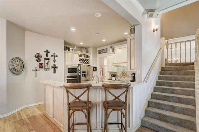 kitchen with custom range hood, light wood-style flooring, a peninsula, appliances with stainless steel finishes, and cream cabinets