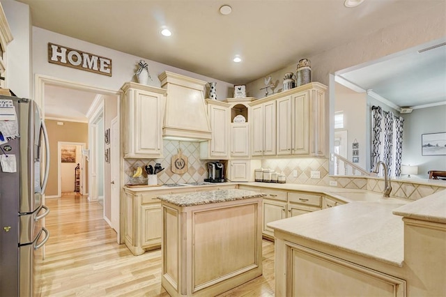 kitchen with ornamental molding, a sink, stainless steel fridge, a peninsula, and custom exhaust hood