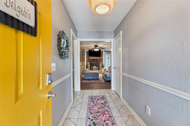 hall with light tile patterned floors, baseboards, a textured ceiling, and a textured wall