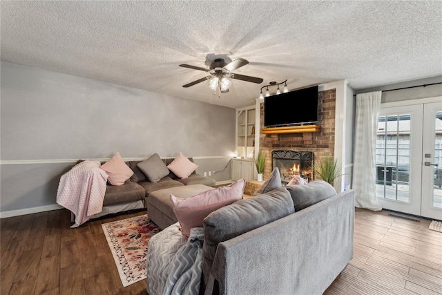 living area with a fireplace, a textured ceiling, french doors, and wood finished floors