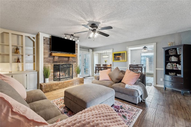 living room featuring a textured ceiling, a brick fireplace, wood finished floors, and a ceiling fan