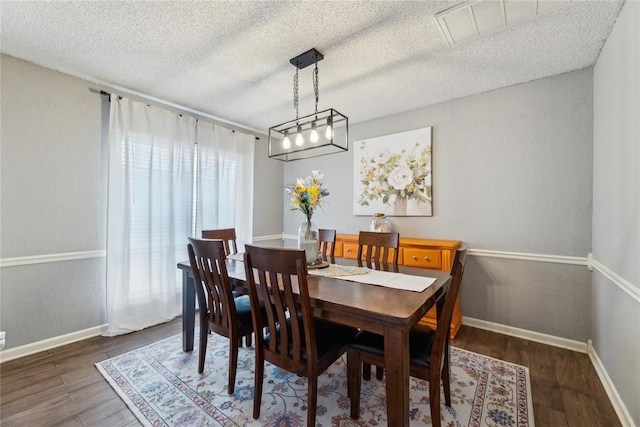 dining space with wood finished floors, baseboards, a textured wall, and a textured ceiling