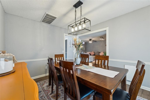 dining area featuring visible vents, baseboards, a textured ceiling, and wood finished floors