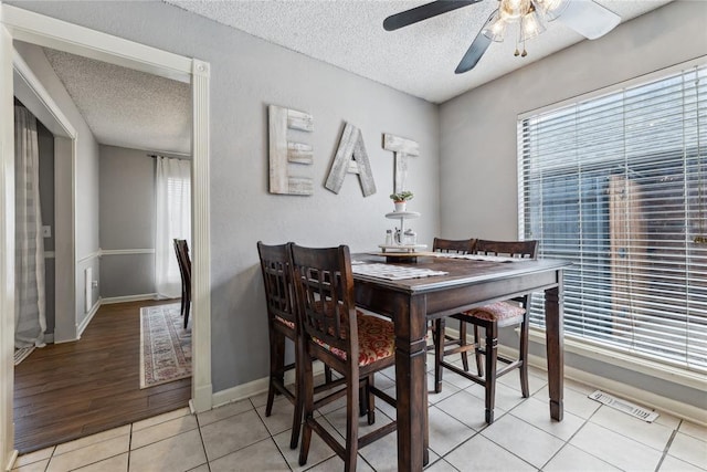 dining space featuring visible vents, baseboards, ceiling fan, light tile patterned flooring, and a textured ceiling