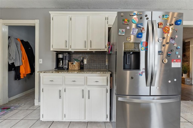 kitchen with tasteful backsplash, light tile patterned flooring, light stone countertops, and stainless steel fridge