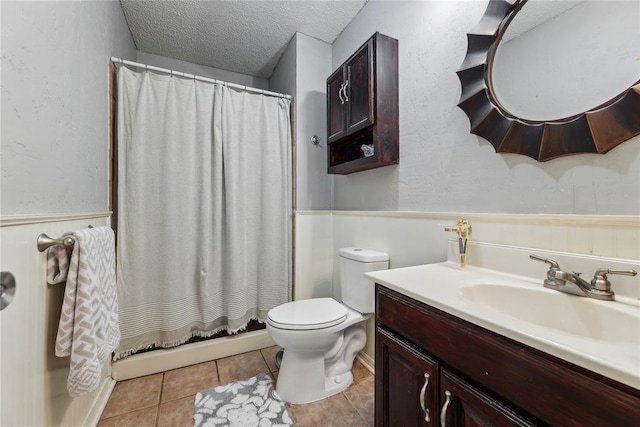 bathroom with a wainscoted wall, toilet, vanity, tile patterned floors, and a textured ceiling