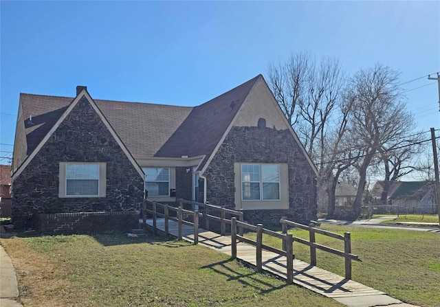 english style home with stone siding and a front lawn