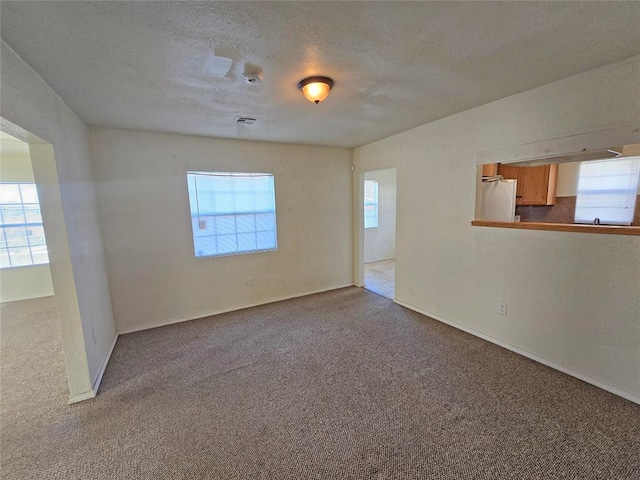 carpeted empty room with a textured ceiling, visible vents, and a wealth of natural light