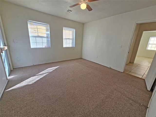 tiled spare room featuring ceiling fan, carpet floors, and visible vents