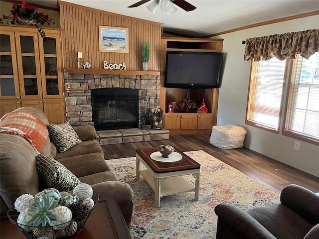 living room featuring wood finished floors, a ceiling fan, lofted ceiling, a stone fireplace, and crown molding