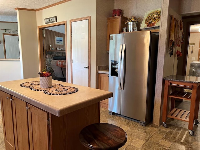 kitchen with brown cabinets, a textured ceiling, stainless steel refrigerator with ice dispenser, and crown molding