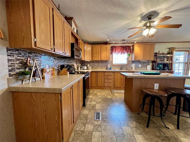 13132 Bluebird Ln, Kingston, OK 73439 - kitchen featuring a breakfast bar area, decorative backsplash, light countertops, stainless steel microwave, and black electric range oven