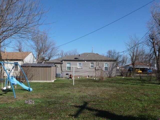 back of property with an outbuilding, fence, a yard, central air condition unit, and a playground